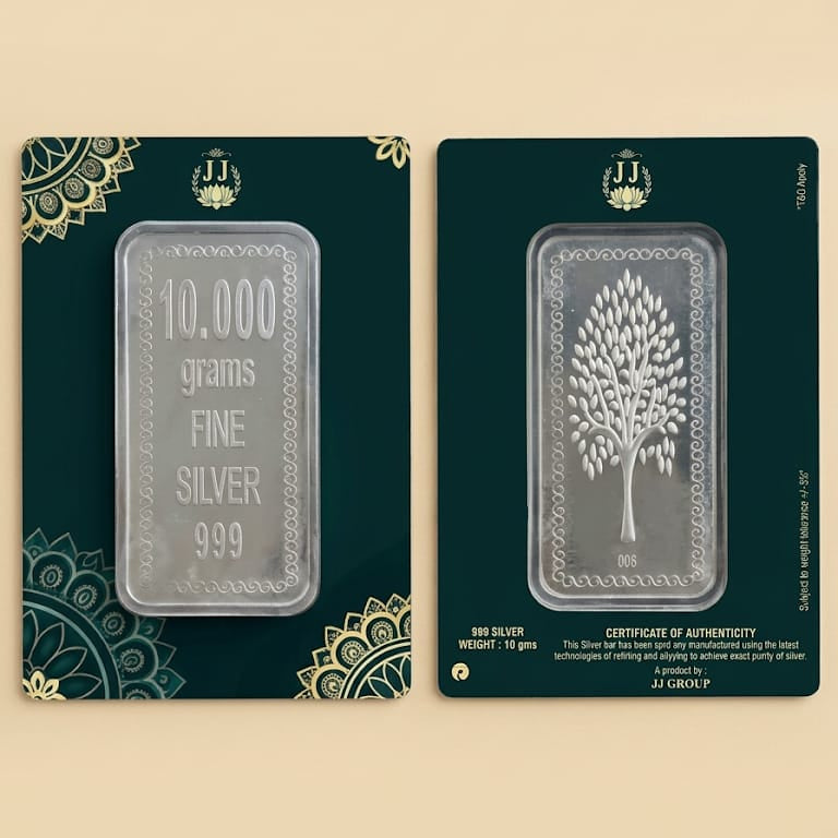 Two JJ Gold Pure silver bars in dark green and gold ornate packaging, displayed side-by-side on a beige background. The left bar is 10,000 grams (10 kg) and features a Sanskrit mantra, while the right bar is 900 grams (1 oz) and features a tree of life.