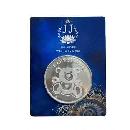 A silver baby shower coin featuring an engraved teddy bear design, mounted on a dark blue display card with the brand initials 'JJ' and product details.